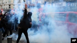 Masked protestors throw debris at riot police amid tear gas smoke during a demonstration Saturday, Jan. 11, 2020 in Lille, northern France.