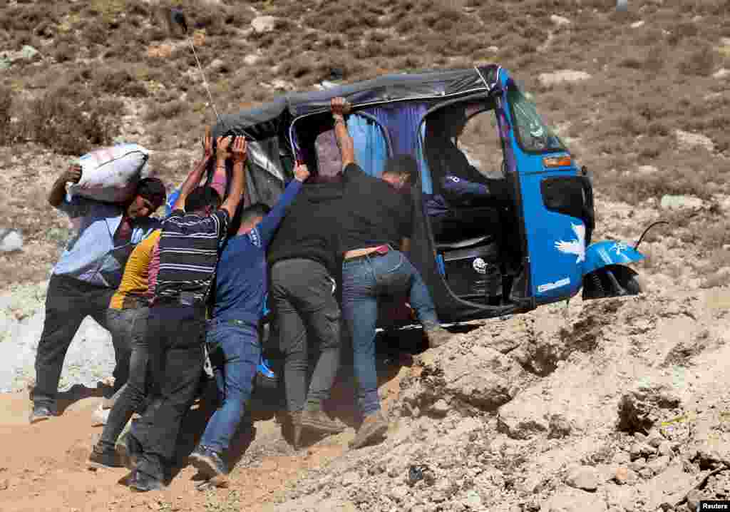 Orang-orang mendorong sebuah tuk-tuk (bajaj) saat menyeberang dari Lebanon ke Suriah, untuk melarikan diri dari peperangan antara Hizbullah dan pasukan Israel, di persimpangan perbatasan Masnaa, Lebanon. (Reuters)&nbsp;