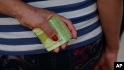 FILE - A woman holds a wad of bills to pay her bus fare in Caracas, Venezuela, Feb. 7, 2018. 