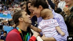 FILE - Michael Phelps celebrates winning his gold medal in the men's 200-meter butterfly with his fiance Nicole Johnson and baby Boomer during the swimming competitions on Aug. 9 at the 2016 Summer Games. Four month after getting married on June 13, the couple celebrated in Mexico.