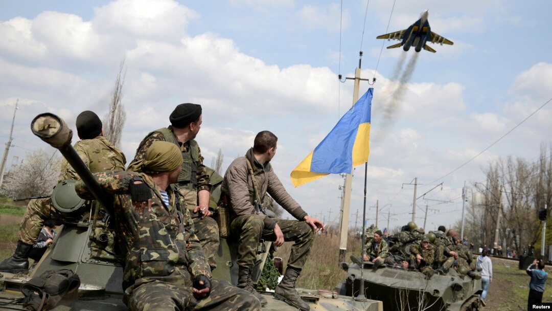 Ukrainian servicemen look at a Ukrainian military jet fly above them while they sit on top of armored personnel carriers in Kramatorsk, Ukraine, April 16, 2014. 