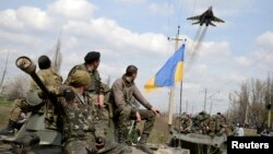 Ukrainian servicemen look at a Ukrainian military jet fly above them while they sit on top of armored personnel carriers in Kramatorsk, Ukraine, April 16, 2014. 