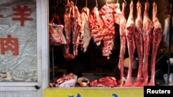 A Chinese vendor reads as she waits for customers inside a butcher shop at a market in Beijing, Feb. 25, 2013. 