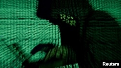 FILE - A man holds a laptop computer as cyber code is projected on him in this illustration picture taken on May 13, 2017. 