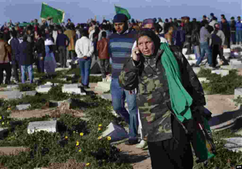 In this image taken during an organized trip by the Libyan authorities, a Libyan woman holding an automatic rifle speaks on the phone as men gather around the grave of a man being buried in Tripoli, Sunday March 20, 2011. The cause of death was unknown. 