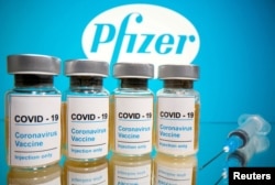 Vials with a sticker reading, "COVID-19 / Coronavirus vaccine / Injection only" and a medical syringe are seen in front of a displayed Pfizer logo, Oct. 31, 2020.