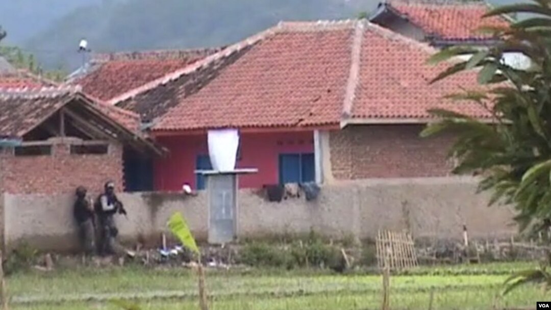 Dua petugas Densus 88 sedang mengintai rumah bercat merah (kanan) yang di dalamnya berisi empat tersangka teroris (foto: Wulan/VOA).