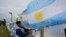 A man ties an Argentine flag carrying solidarity messages to a fence at the Mar de Plata Naval Base after the navy announced a sound detected during the search for the missing ARA San Juan submarine was consistent with that of an explosion, in Mar de Plat