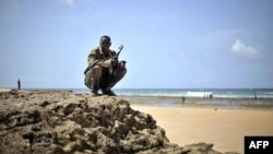 A handout picture released by the African Union-United Nations Information Support Team shows an armed man squatting at a beach during a demonstration by a local militia, formed in order to provide security in the town of Marka, April 30, 2014.
