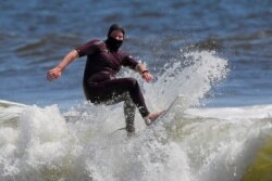 In this May 13, 2020, file photo, Tim O'Rourke surfs with a face covering to protect him from the coronavirus at Venice Beach, during the coronavirus outbreak in Los Angeles.