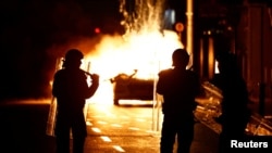 Polisi berjaga di sebuah mobil polisi yang terbakar dekat lokasi penikaman yang mengakibatkan sejumlah anak terluka di Dublin, Irlandia, Kamis, 23 November 2023. (Foto: Clodagh Kilcoyne/Reuters)