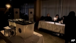 Election officials assist voters with mobile phone flashlights during a power failure in Chisinau, Moldova, Oct. 20, 2024.