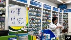 Pharmacist Liu Zhuzhen stands near a sign reading "face masks are sold out" at her pharmacy in Shanghai, China, Jan. 21, 2020.