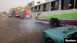 FILE - A bus leaves as smoke is seen at a bus park in Abuja, Nigeria, February 1, 2017. 