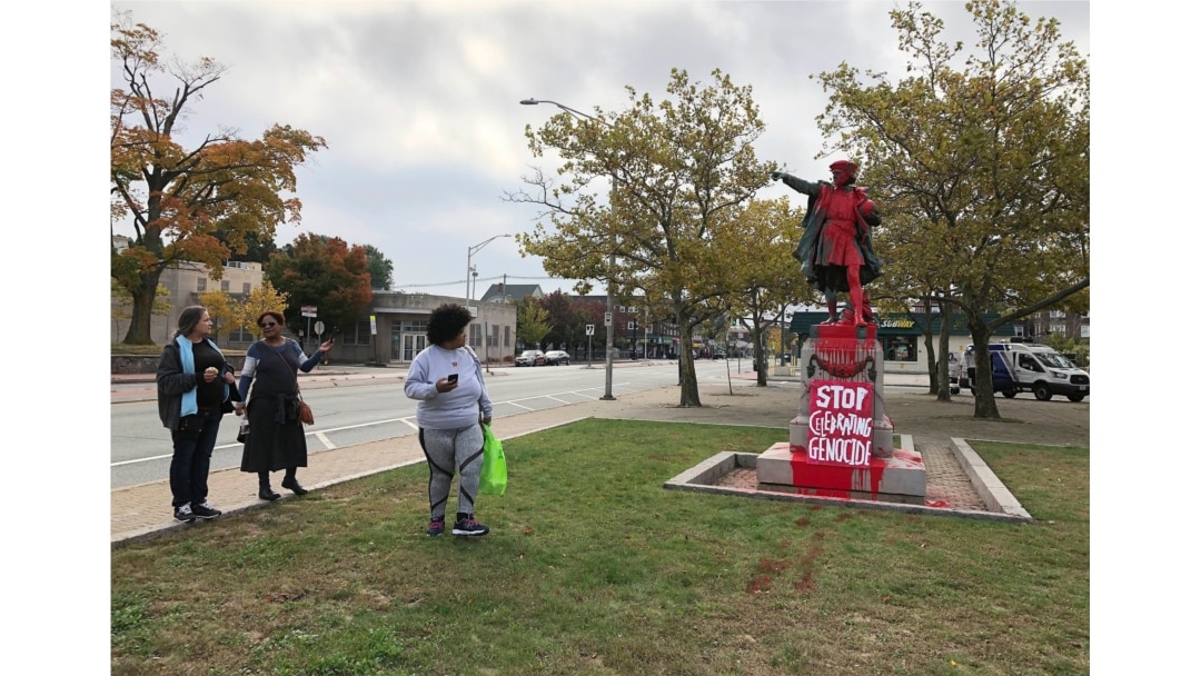 People stop to view red paint covering a statue of Christopher Columbus on Monday, Oct. 14, 2019, in Providence, R.I., after it was vandalized on the day named to honor him as one of the first Europeans to reach the New World.