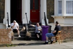 People sit and talk outside flats and houses near Victoria Park, east London on April 11, 2020, as life in Britain continues over the Easter break, during the nationwide lockdown to combat the novel coronavirus pandemic.