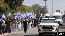 Israelitas agitam a bandeira nacional enquanto o comboio de veículos que transporta os corpos dos quatro reféns israelitas entregues pelo Hamas chega à entrada do Centro Nacional de Medicina Legal em Telavive, a 20 de fevereiro de 2025.