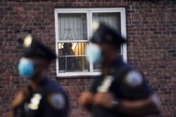 FILE - In this Aug. 18, 2020, file photo, a neighbor watches New York City Police Department officers work a crime scene where several young men were shot and wounded in the Queens borough of New York.