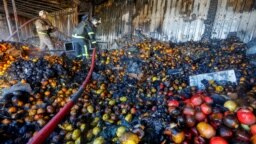 Los bomberos se paran sobre montones de frutas mientras trabajan dentro de los puestos de mercado quemados y golpeados por los bombardeos en el transcurso del conflicto entre Rusia y Ucrania en Donetsk, Ucrania controlada por Rusia, el 6 de diciembre de 2022.