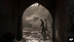 FILE - Construction workers carry a generator as a bulldozer remove debris from destroyed shops in the Old City of Mosul, Iraq, Nov. 18, 2017. 