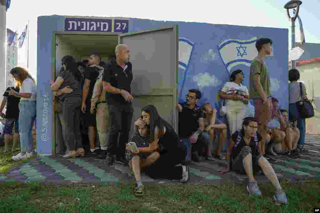 Israelis take cover next to a shelter as a siren sounds a warning of incoming rockets fired from Lebanon, in Nahariya, northern Israel.