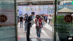 A woman displays her phone to doorman, to confirm using a mobile application to help contact-tracing at the entrance to the upmarket shopping mall Siam Paragon in Bangkok, Thailand, May 17, 2020.
