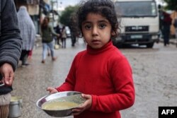 FILE - A displaced Palestinian child carries a ration of red lentil soup, distributed by volunteers in Rafah in the southern Gaza Strip on February 18, 2024, amid the ongoing conflict between Israel and the militant group Hamas.