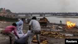 People place the body of a man who died from COVID-19 on a pyre before his cremation on the banks of the river Ganges at Garhmukteshwar in the northern state of Uttar Pradesh, India, on May 6, 2021.