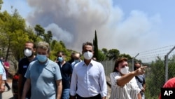 Greece's Prime Minister Kyriakos Mitsotakis, center, accompanied by Culture Minister Lina Mendoni, right, and Minister for Citizen Protection Michalis Chrisochoidis, left, visit the ancient Olympia during a wildfire in western Greece, Aug. 5, 2021.