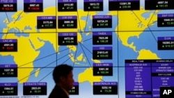 A man walks past a bank's electronic board showing the share indexes around the world at the Hong Kong Stock Exchange, Aug. 27, 2015.