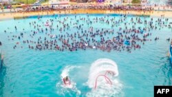 People watch a flyboard performance as they cool off in a swimming pool in Lianyungang, in China&#39;s eastern Jiangsu province, July 4, 2021.