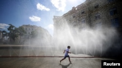 FILE - A child runs under water sprinklers during a heat wave in Vienna, Austria, July 23, 2019. 