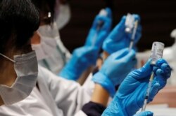 FILE - Health care workers prepare doses of the Moderna coronavirus vaccine before administering them to staffers of Japan's supermarket group Aeon at the company's shopping mall in Chiba, Japan, June 21, 2021.