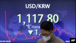 A currency trader walks by the screen showing the foreign exchange rate between U.S. dollar and South Korean won at the foreign exchange dealing room in Seoul, South Korea, Feb. 9, 2021.
