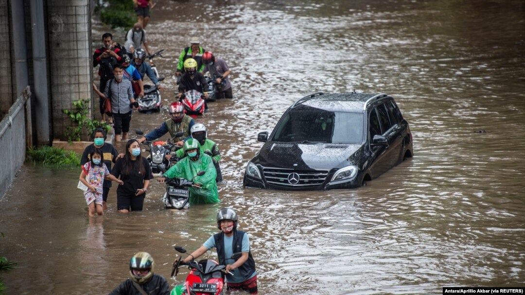 Warga mendorong sepeda motornya melewati air di daerah terdampak banjir menyusul hujan deras di Jakarta, 20 Februari 2021. (Foto: Antara/Aprillio Akbar via REUTERS)