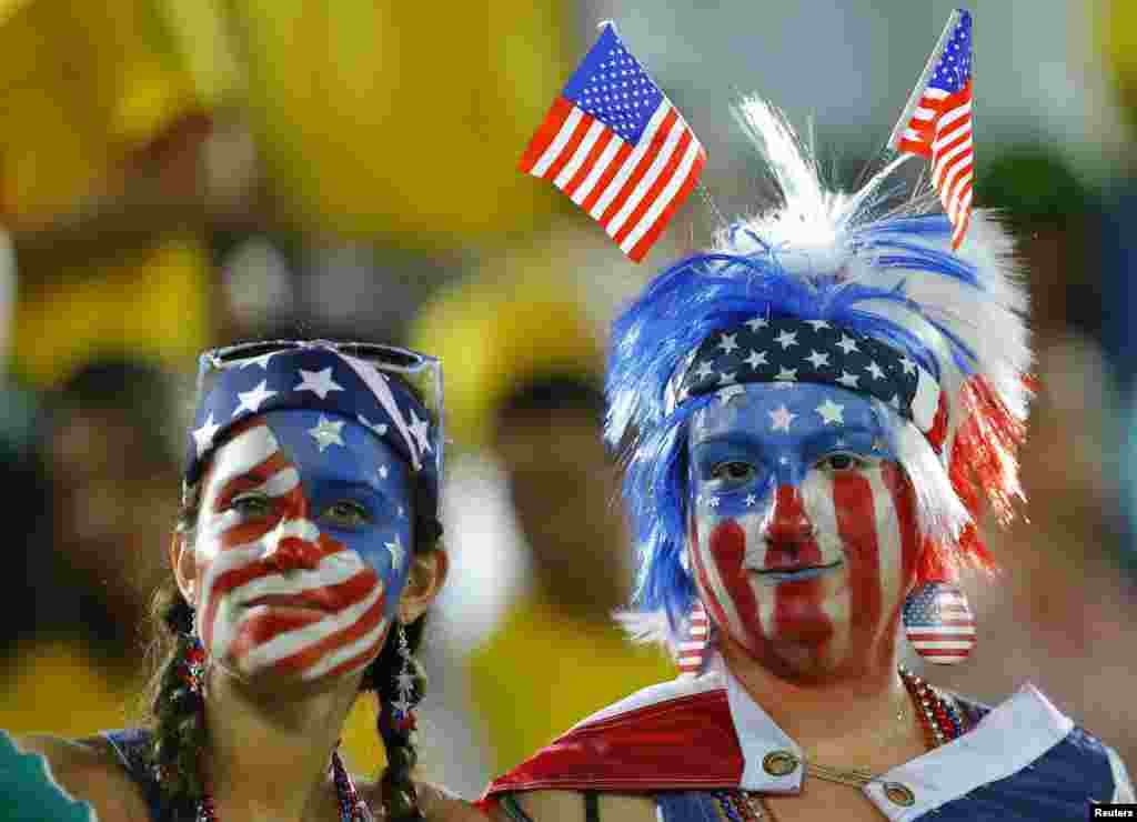 Dua penggemar tim AS dengan hiasan wajah dan rambut mengikuti bendera Amerika saat menonton pertandingan melawan Ghana di stadion Dunas, Natal di Brazil (16/6). (Reuters/Brian Snyder)