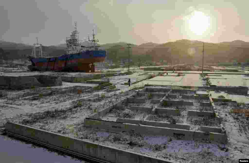 A local resident and a dog walk near a ship brought ashore by the March 11, 2011 tsunami and earthquake in Kesennuma, Miyagi Prefecture, Japan, March 11, 2013.