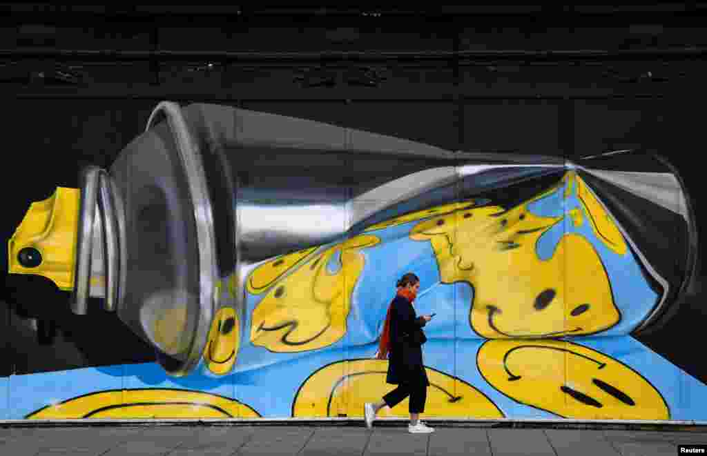 A woman looks at her phone as she walks past street art on a wall in London, Britain.