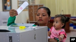 FILE - In this Sunday, Feb. 25, 2018, file photo, a woman holds a child as she casts a ballot in Kandal province, southeast of Phnom Penh, Cambodia. Cambodia's National Election Committee has warned that anyone urging voters to boycott the upcoming genera