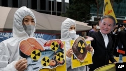 Environmental activists wearing a mask of Japanese Prime Minister Yoshihide Suga and protective suits perform to denounce the Japanese government's decision on Fukushima water, near the Japanese embassy in Seoul, South Korea, April 13, 2021.