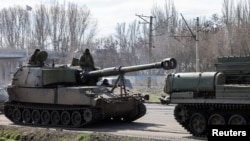 A self-propelled howitzer is towed through a street in Kostiantynivka