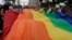 Para peserta pawai memamerkan bendera pelangi besar saat mengikuti pawai LGBT, Gay Pride Parade, di Quito, Ekuador, Sabtu, 29 Juni 2019. (Foto: AP)