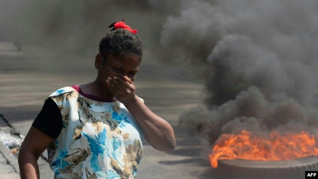 Una mujer camina junto a neumáticos en llamas durante una manifestación tras la renuncia del primer ministro, Ariel Henry, en Puerto Príncipe, Haití, el 12 de marzo de 2024.