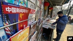 FILE - A newsstand vendor looks through his display near a magazine with a cover depicting U.S. President Joe Biden near U.S. and Chinese flags in Beijing on Jan. 21, 2021.