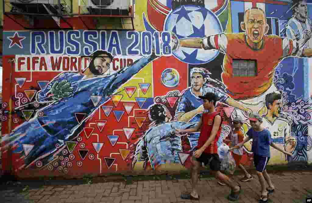 Beberapa anak laki-laki berjalan melewati mural para pesepak bola untuk mempromosikan Piala Dunia 2018 di Rusia, di pinggiran Jakarta, 12 Juni 2018. (Foto: AP)