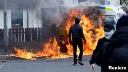 Dissident republicans stand near a burning police car after an anti-Good Friday Agreement rally on the 25th anniversary of the peace deal, in Londonderry, Northern Ireland, April 10, 2023.