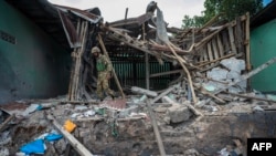 FILE - Members of the Mandalay Peoples Defense Forces (MDY-PDF) walk through a structure bombed by a Myanmar military aircraft near the front line amid clashes in northern Shan State, Dec. 11, 2023.