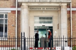 FILE - Men wearing face masks chat at the entrance of the Fondation Rothschild nursing home, in Paris, March 27, 2020.