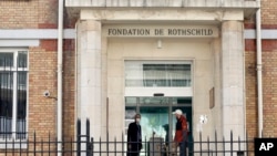 Men wearing face masks at the entrance of the Fondation Rothschild nursing home, in Paris, March 27, 2020. Governments in Europe's hardest-hit countries have yet to systematically test the residents of nursing homes.