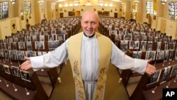 FILE - The Rev. Nicolas Sanchez Toledano poses among pews adorned with portraits of his parishioners at St. Patrick's Catholic Church during the coronavirus outbreak in the North Hollywood section of Los Angeles, May 22, 2020.